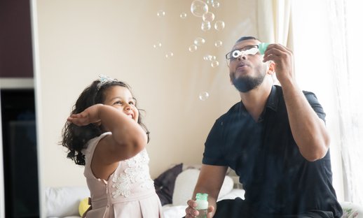 Dad and young girl playing with bubbles at home