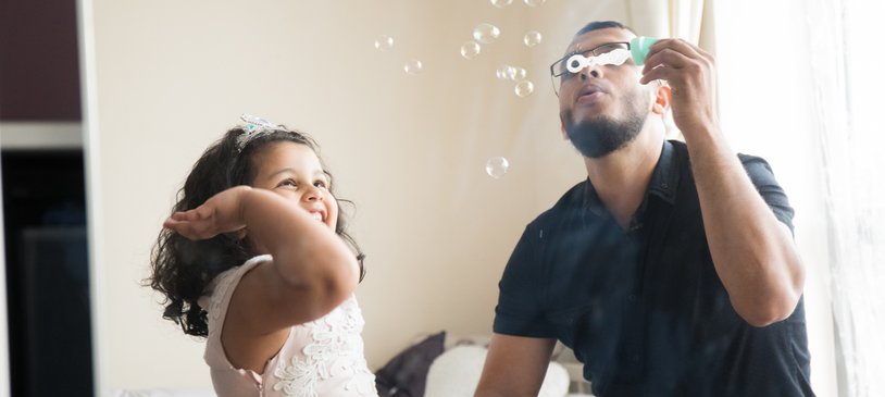 Dad and young girl playing with bubbles at home