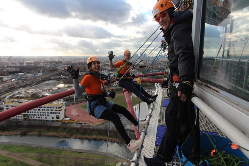 Two people waving to camera while at the top of the tower. They are about to abseil.