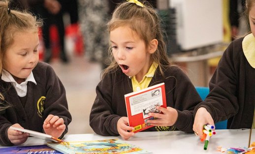 Two primary school children look at books excitedly as part of the Young Readers Programme