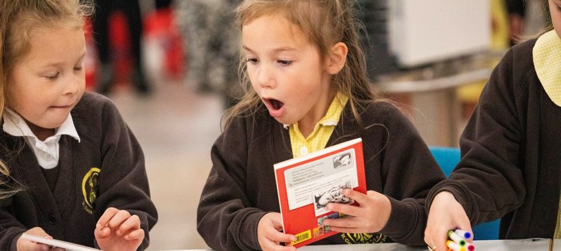 Two primary school children look at books excitedly as part of the Young Readers Programme