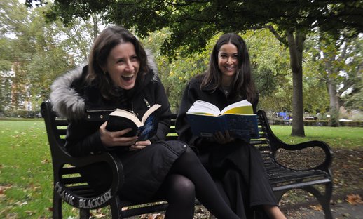 Two women enjoying reading on a park bench