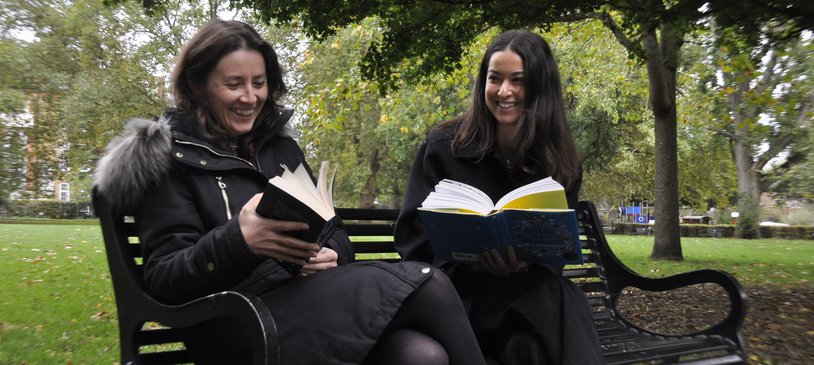 Two women enjoying reading on a park bench