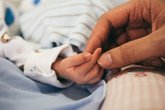 A parent reaches for a newborn's tiny hand