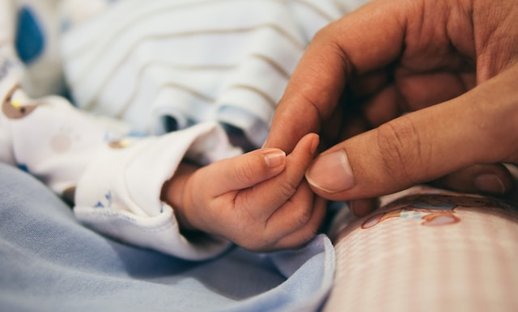 A parent reaches for a newborn's tiny hand