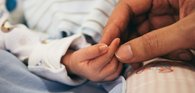 A parent reaches for a newborn's tiny hand